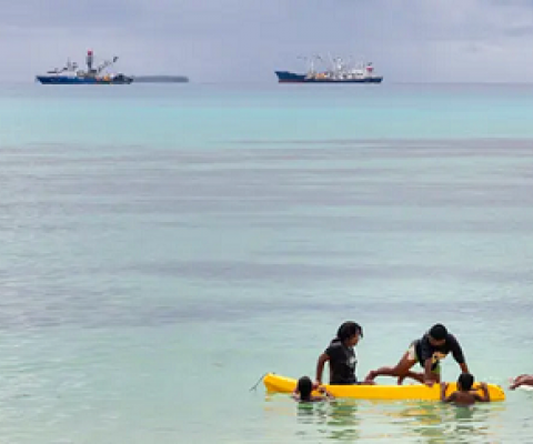 Children play in a small boat as large fishing boats sit offshore in Vanuatu. Photograph: Sean Gallagher/The Guardian